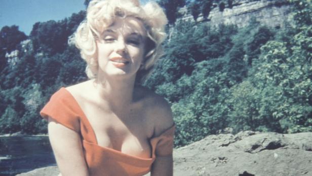 Marilyn Monroe posiert in einem roten Kleid vor einer grünen Landschaft.