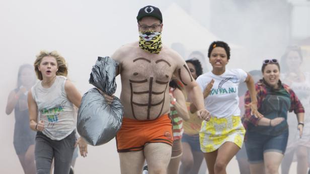 Szene aus „Bad Neighbors 2“ mit Seth Rogen, der mit aufgemalten Bauchmuskeln und Müllsack vor einer Gruppe Studenten herläuft.