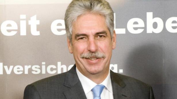Ein Mann mit grauem Haar und Schnurrbart trägt einen Anzug.