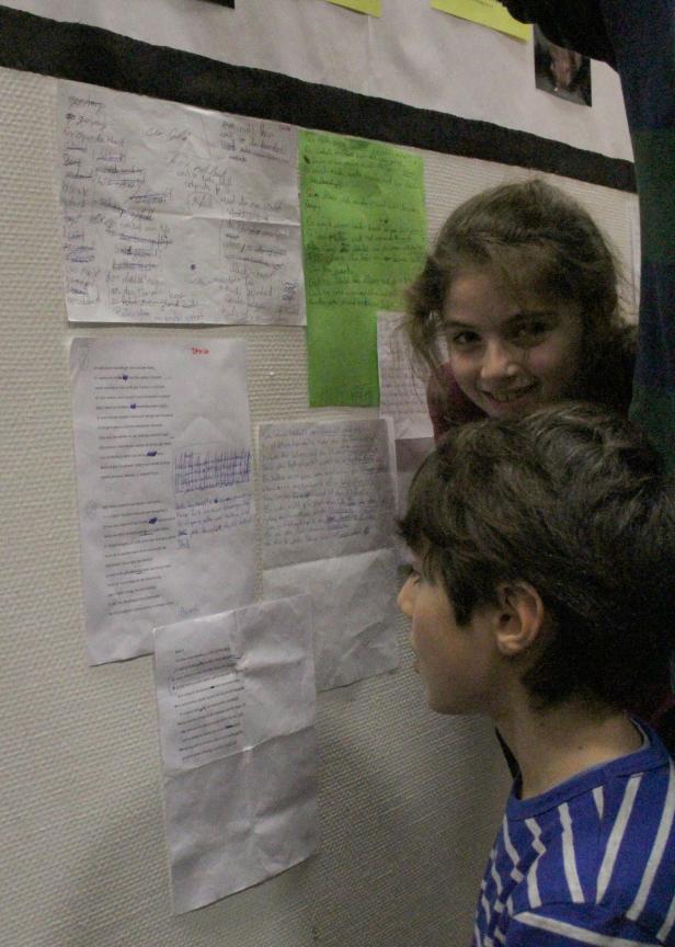 Zwei Kinder betrachten Zettel mit handschriftlichen Texten an einer Wand.