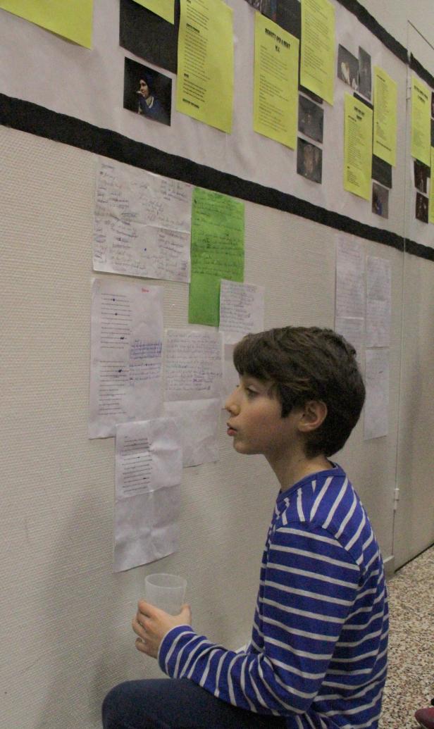 Ein Junge betrachtet Zettel an einer Wand und hält einen Becher.