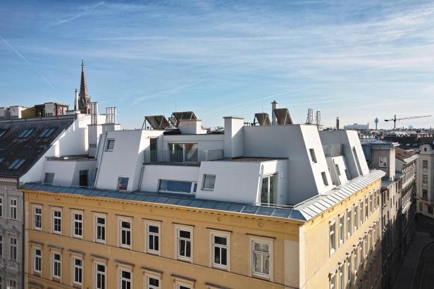 Blick auf ein gelbes Gebäude mit Dachausbau und die Wiener Skyline.