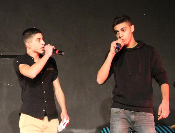 Zwei junge Männer stehen auf einer Bühne und singen in Mikrofone.