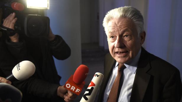 Ein Mann mit grauen Haaren spricht in mehrere Mikrofone.