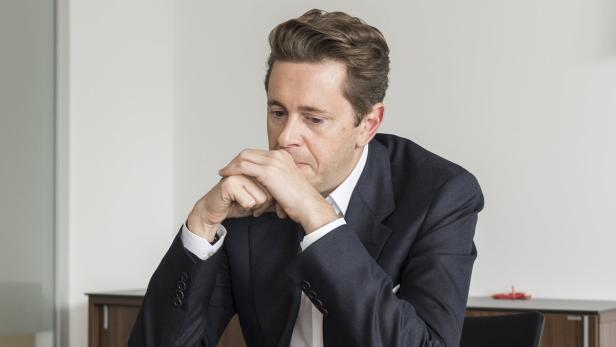 Ein Mann im Anzug sitzt an einem Tisch und wirkt nachdenklich.