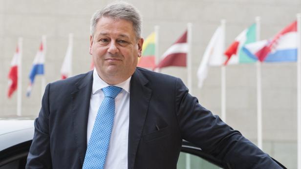 Ein Mann im Anzug steht vor einer Reihe von Flaggen.