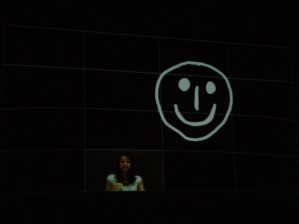 Eine Frau steht vor einer Leinwand mit einem Smiley-Gesicht.
