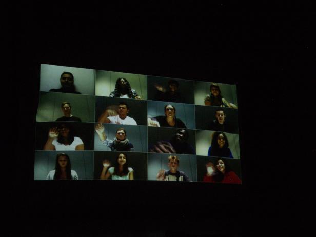 Ein Bildschirm zeigt eine Videokonferenz mit mehreren Personen, die winken.