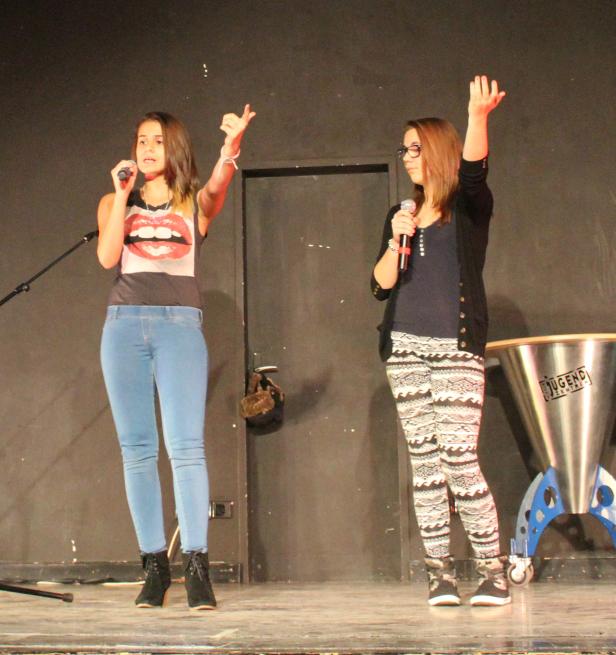 Zwei junge Frauen stehen auf einer Bühne und singen in Mikrofone.