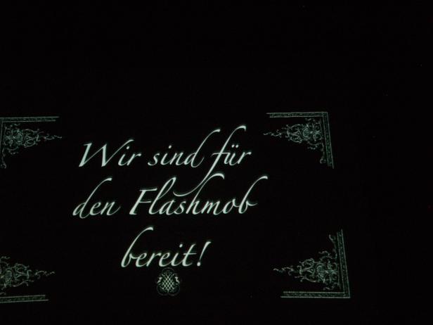 Der Schriftzug „Wir sind für den Flashmob bereit!“ auf schwarzem Hintergrund mit Ornamenten.