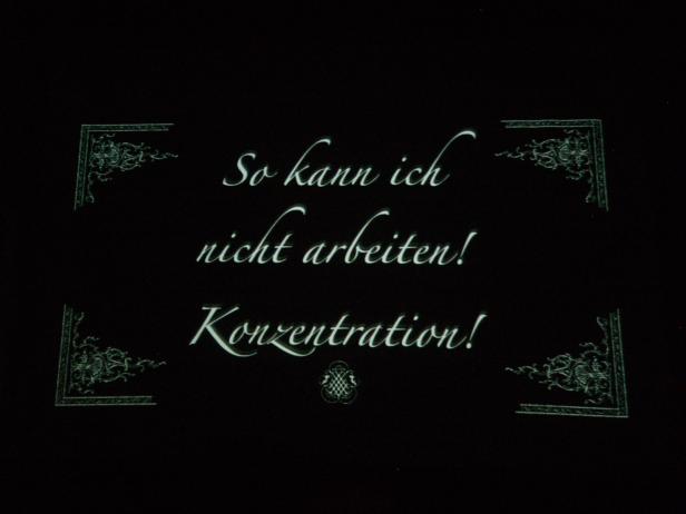 „So kann ich nicht arbeiten! Konzentration!“ steht auf einer dunklen Tafel.