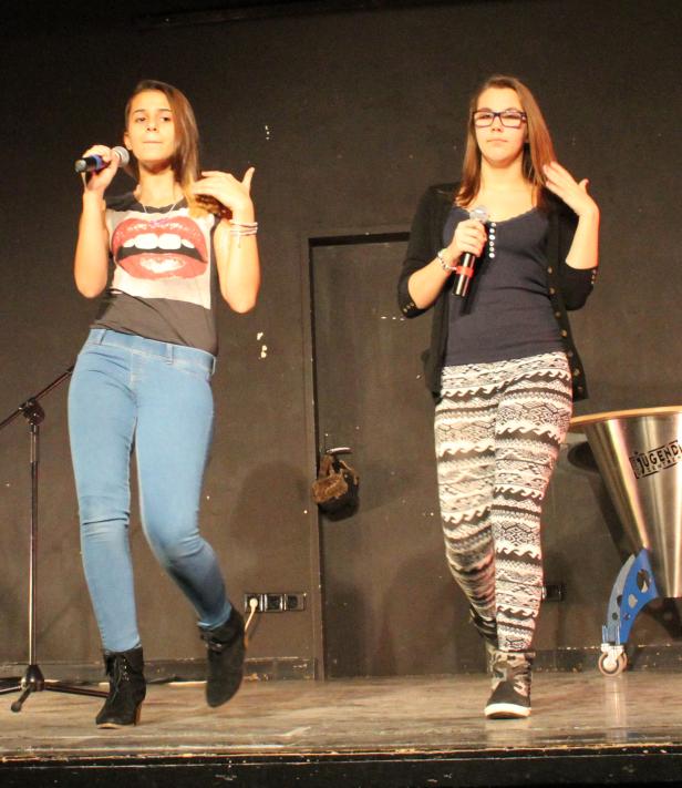 Zwei junge Frauen treten mit Mikrofonen auf einer Bühne auf.