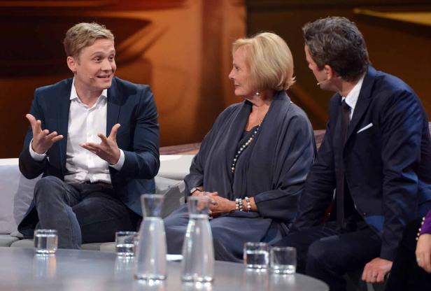 Drei Personen sitzen auf einer Couch und unterhalten sich während einer Talkshow.