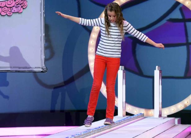 Ein Mädchen balanciert mit ausgestreckten Armen auf einem schmalen Steg.