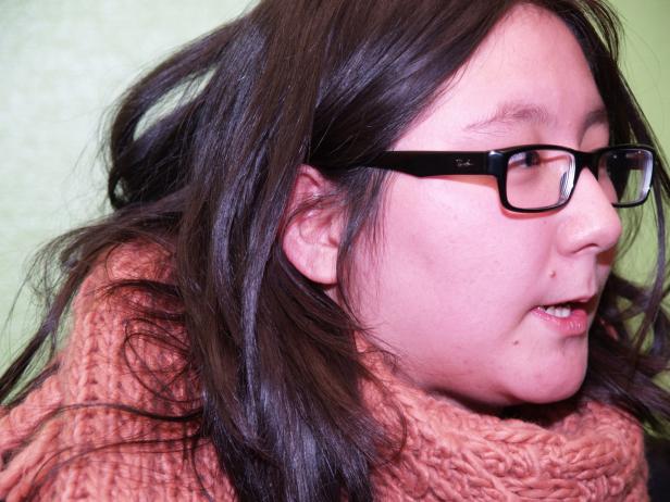 Eine junge Frau mit Brille und einem orangefarbenen Schal blickt zur Seite.