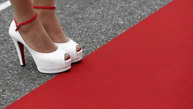 Weiße High Heels mit roten Akzenten auf einem roten Teppich.