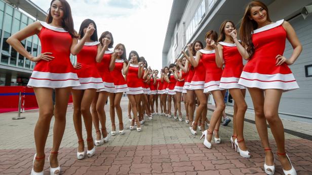 Eine lange Reihe junger Frauen in roten Kleidern und weißen High Heels posiert.