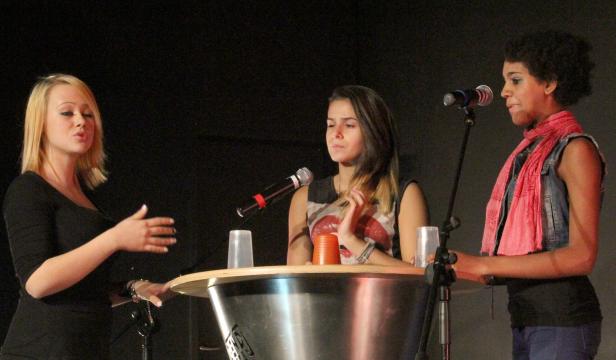 Drei Frauen stehen an einem Tisch mit Mikrofonen und sprechen.