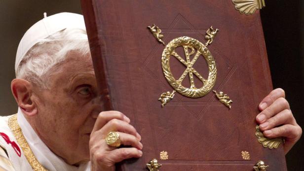 Papst Benedikt XVI. hält ein verziertes, ledergebundenes Buch vor sein Gesicht.