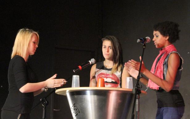 Drei junge Frauen stehen auf einer Bühne und klatschen.