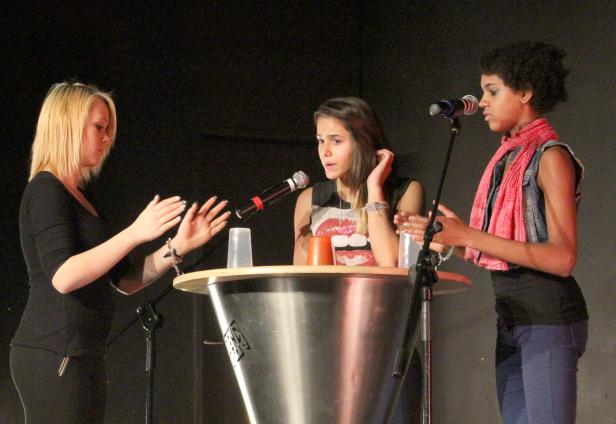 Drei Frauen stehen auf einer Bühne hinter einem Rednerpult und sprechen in Mikrofone.