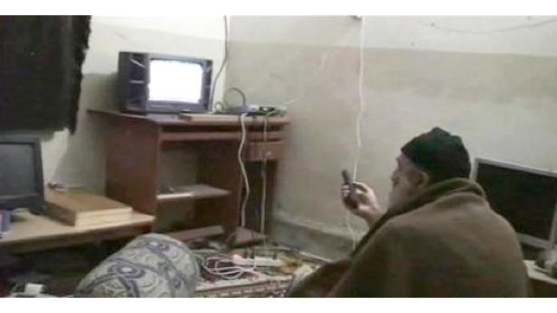 Ein Mann mit Bart und Mütze sitzt in einem Raum und bedient einen alten Fernseher.