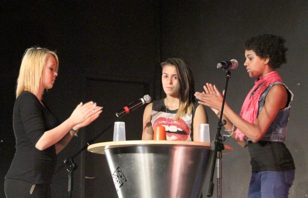 Drei Frauen stehen an einem Podium und klatschen Applaus.