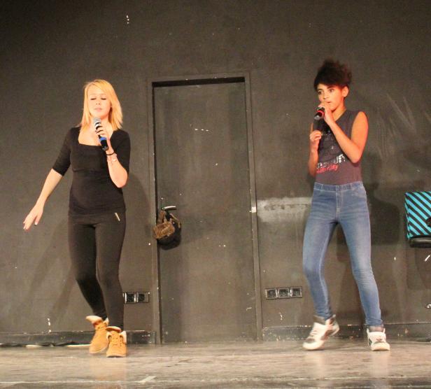 Zwei Sängerinnen treten auf einer Bühne mit Mikrofonen auf.