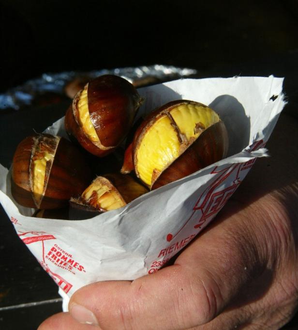 Eine Hand hält eine Papiertüte mit gerösteten Maronen.