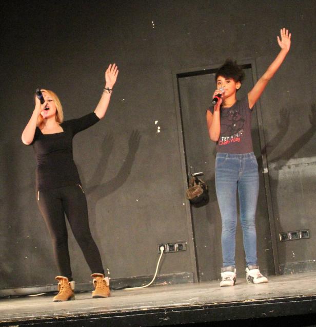 Zwei junge Frauen stehen auf einer Bühne und singen in Mikrofone.