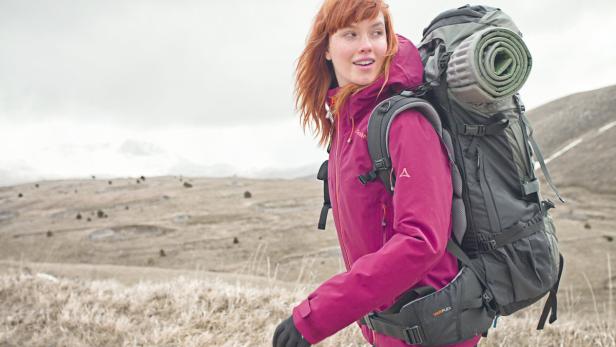 Eine Frau mit rotem Haar wandert mit einem großen Rucksack durch eine hügelige Landschaft.