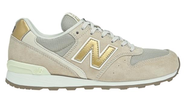 Ein beiger New Balance Sneaker mit goldenem „N“-Logo an der Seite.