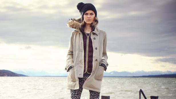 Eine Frau mit Mütze und Mantel steht an einem See.