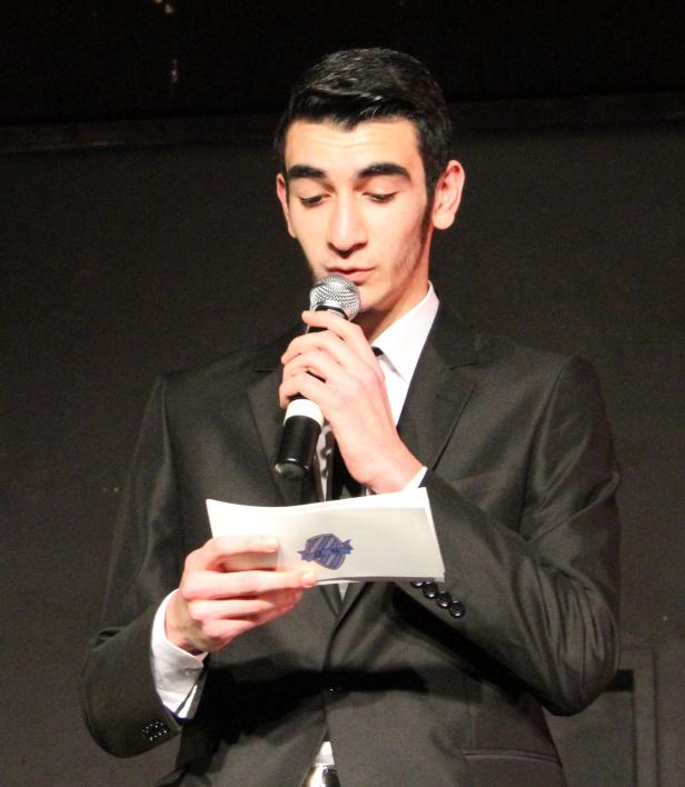 Ein junger Mann im Anzug liest von einem Blatt Papier und spricht in ein Mikrofon.