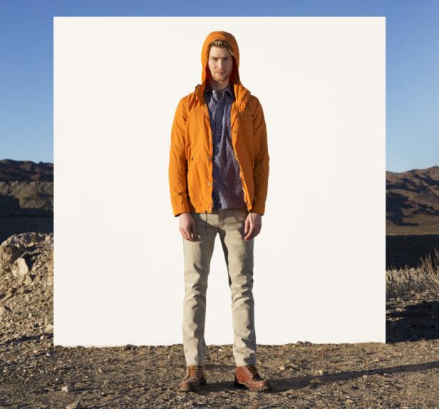 Ein Mann mit orangefarbener Jacke steht vor einer weißen Wand in einer Wüstenlandschaft.