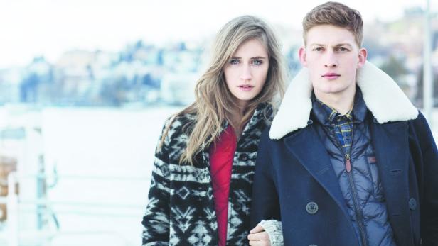 Ein junges Paar in Winterkleidung steht vor einer verschneiten Landschaft.