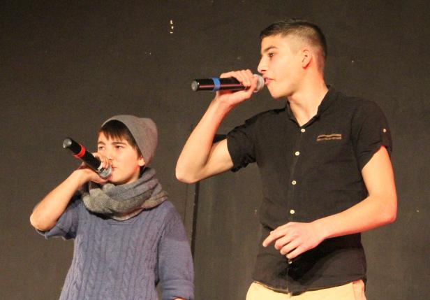 Zwei junge Männer rappen mit Mikrofonen auf einer Bühne.