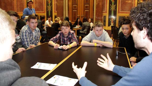 Eine Gruppe Jugendlicher sitzt an einem Tisch und hört aufmerksam zu.