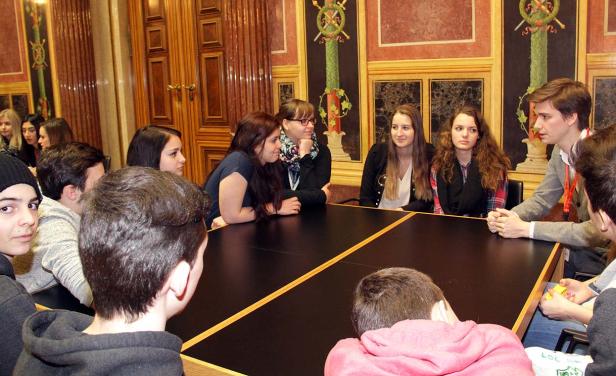 Eine Gruppe junger Leute sitzt an einem Tisch in einem verzierten Raum.