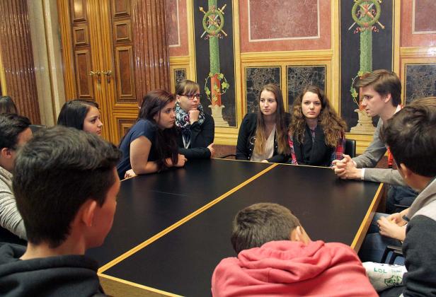 Eine Gruppe junger Leute sitzt an einem Tisch in einem verzierten Raum.