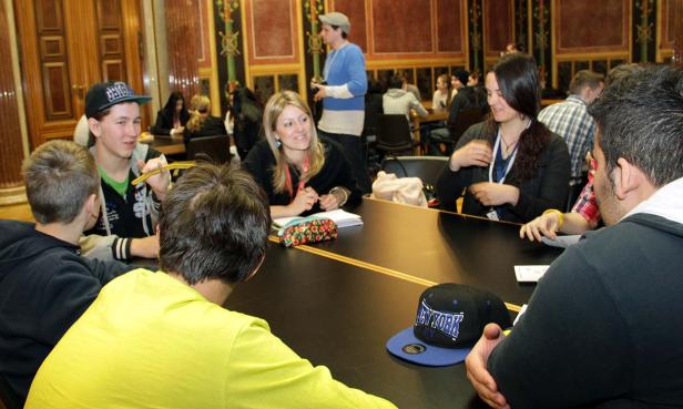 Eine Gruppe junger Leute sitzt an einem Tisch in einem verzierten Raum.