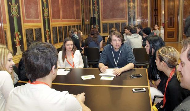 Eine Gruppe junger Leute sitzt an einem Tisch in einem verzierten Raum.