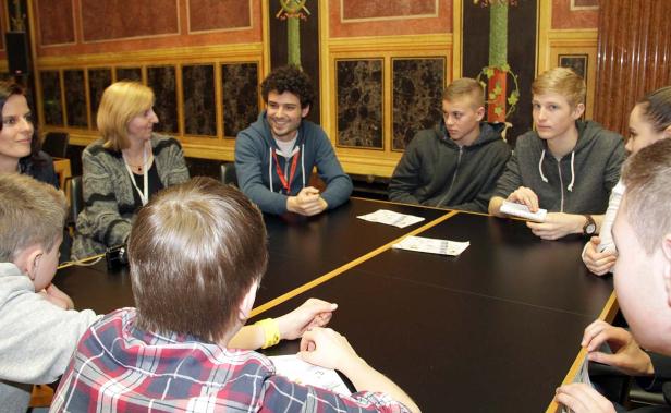Eine Gruppe von Jugendlichen und Erwachsenen sitzt an einem Tisch in einem verzierten Raum.