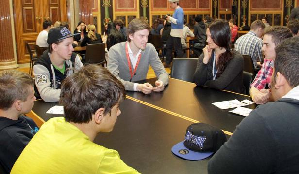 Eine Gruppe junger Leute sitzt an einem Tisch in einem verzierten Raum.