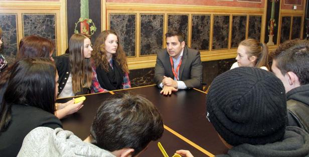 Eine Gruppe junger Leute sitzt mit einem Mann an einem Tisch und diskutiert.