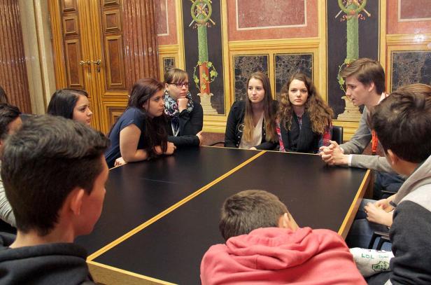 Eine Gruppe junger Leute sitzt an einem Tisch in einem Raum mit Wandmalereien.