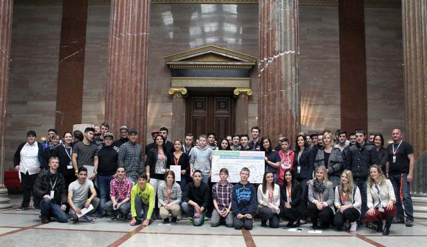 Eine Gruppe junger Menschen posiert mit einem Schild für eine faire Arbeitswelt vor Säulen.