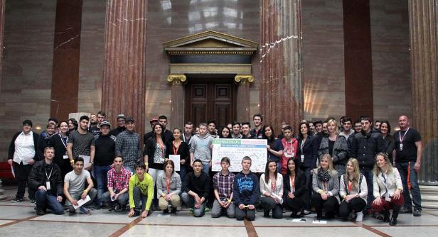 Eine Gruppe junger Leute posiert mit einem Schild für eine faire Arbeitswelt in einem Gebäude mit Säulen.