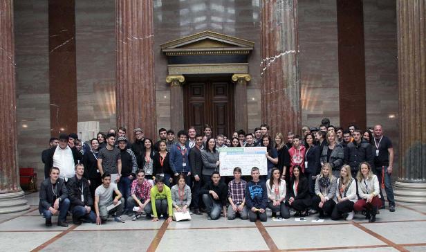 Eine Gruppe von Menschen posiert mit einem Schild mit der Aufschrift „Ideenkatalog für eine faire Arbeitswelt“ vor Säulen.