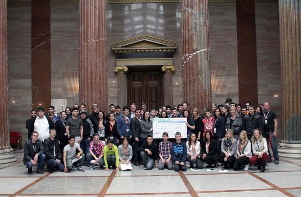 Eine große Gruppe von Menschen posiert mit einem Schild vor einem Gebäude mit Säulen.